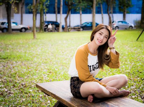 Улыбающаяся девушка азиатка сидит на лавке в парке обои для рабочего