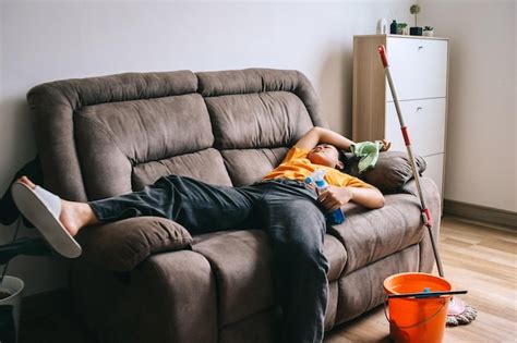 Una joven exhausta que se queda dormida en el sofá sintiéndose cansada después de limpiar la