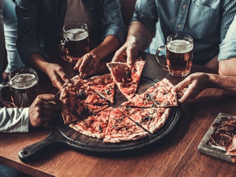 Several People Are Eating Pizza And Drinking Beer