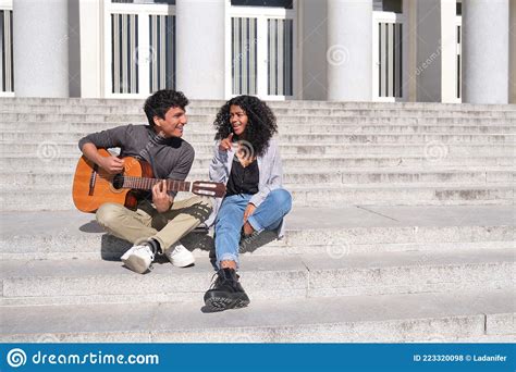 A Young Latin Couple Playing The Guitar And Singing Sitting On Stairs