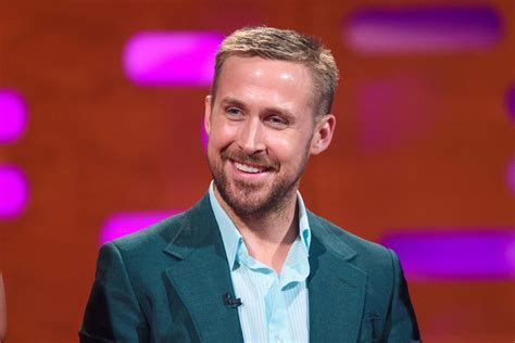 Smiling Ryan Gosling Wearing A Dark And Green Coat And Light Blue Polo