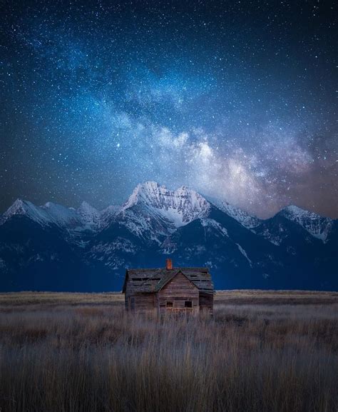 An Old House In The Middle Of A Field Under A Night Sky Filled With Stars