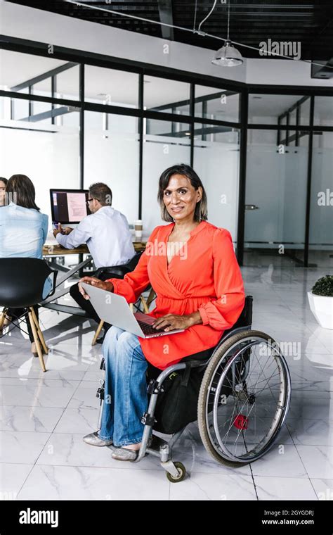 Latin Transgender Woman Sitting In Wheelchair In Modern Office Using