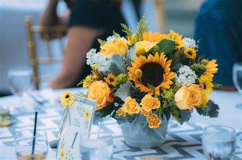 A Vase With Sunflowers And Other Flowers On A White Table Cloth At An Event