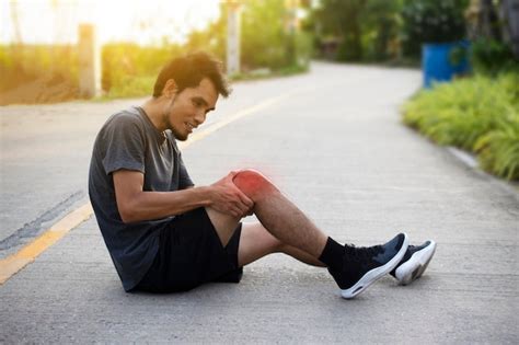 Vista Lateral De Un Hombre Con Dolor De Rodilla Sentado En La Carretera