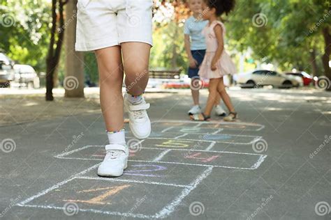 Little Children Playing Hopscotch Drawn With Chalk On Asphalt Outdoors