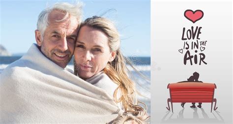 composite image of smiling couple wrapped up in blanket on the beach