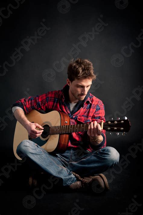 Young Man Playing Guitar Against Black Background Stock Photo