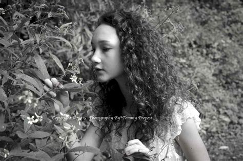 A Woman Standing In Front Of Some Bushes With Her Hand On The Plant S Leaves