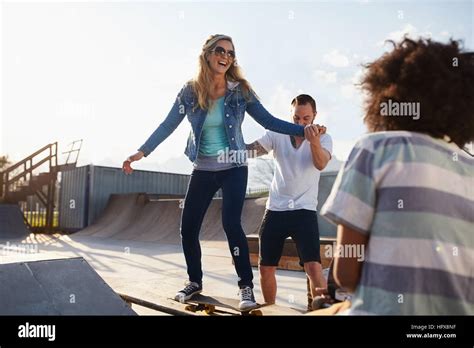 Boyfriend Helping Girlfriend On Skateboard In Sunny Skate Park Stock