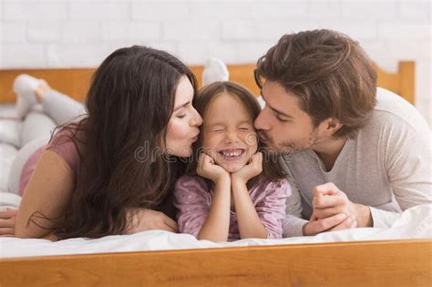 Madre Y Padre Queridos Besando A Su Hija En La Cama Foto De Archivo