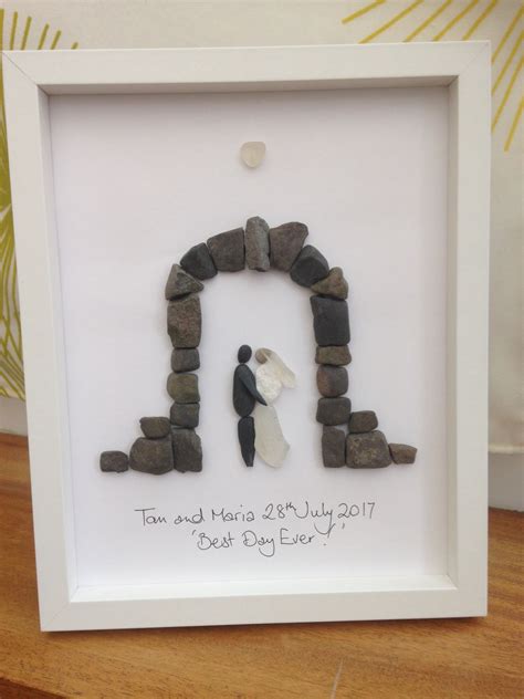A White Frame With Rocks In The Shape Of A House And A Bride And Groom
