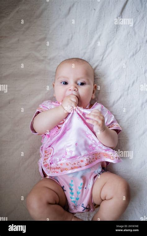 Adorable Baby Girl From Above Biting Her Asian Pink Attire And Lying