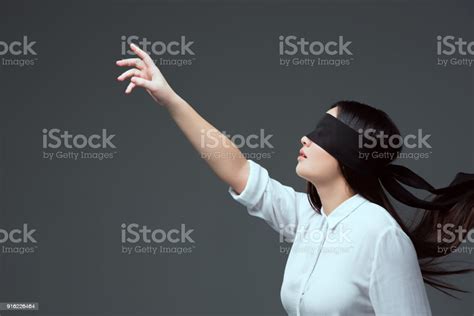 Woman Wearing Black Blindfold And Raising Hand Isolated On Grey Stock