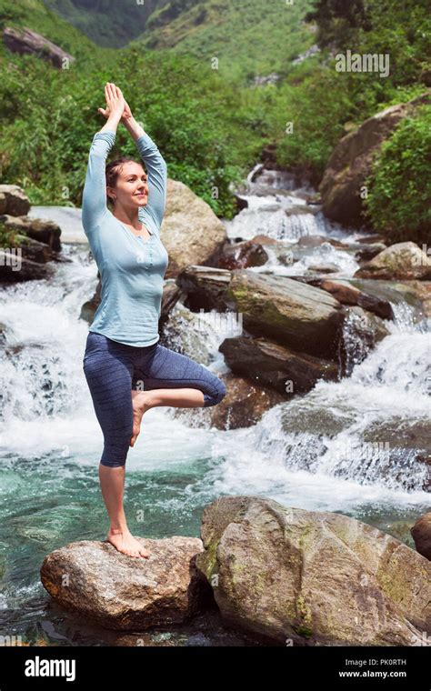 Woman In Yoga Asana Vrikshasana Tree Pose At Waterfall Outdoors Stock