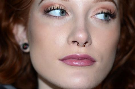 A Close Up Of A Woman With Red Hair And Blue Eyes Wearing Nose Piercings