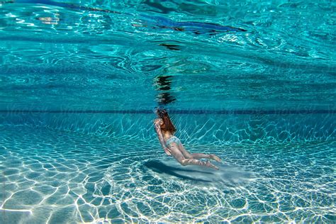 Teenage Girl Floating Underwater In A Large Deep Blue Swimming Pool By