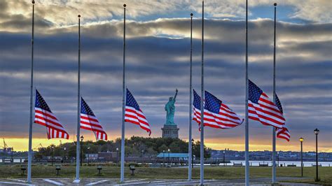 Statue Of Liberty Seen Behind Us Flags At Half Staff For The
