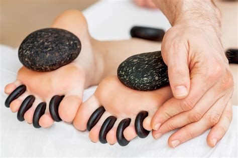 premium photo hands of massage therapist put stones between the toes of woman while stone