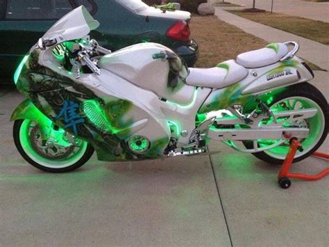 A White And Green Motorcycle Parked On The Side Of A Street Next To A Car