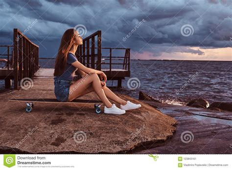 Sensual Girl Sitting On A Skateboard On The Beach Is Enjoying Amazing