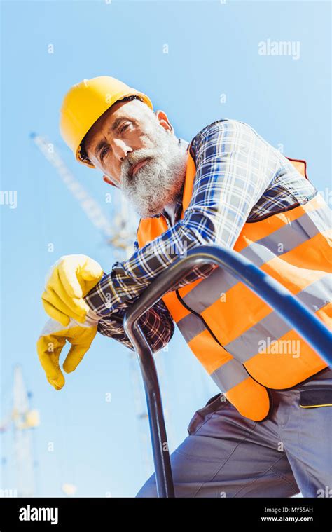 Bearded Construction Worker In Reflective Vest And Hardhat Leaning On