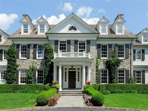 A Large White House With Lots Of Windows And Bushes On The Front Lawn