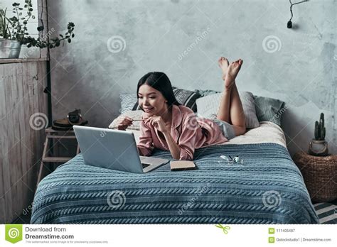 Lazy Day At Home Attractive Young Woman Using Computer And Smiling While Lying On The Bed At