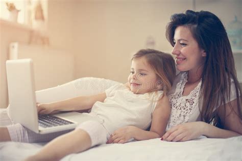 Young Mother With Daughter Using Laptop On Bed At Home Stock Photo