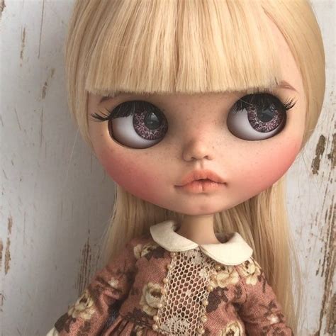 A Doll With Blonde Hair And Big Blue Eyes Wearing A Brown Dress Is