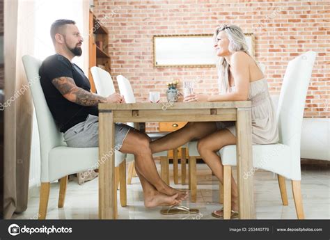 Man And Woman Sitting By Table And Playing With Legs Stock Photo By