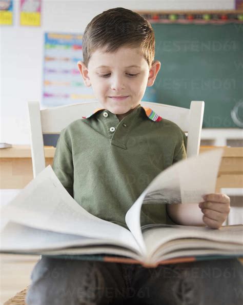 Caucasian Boy Reading Book In Classroom Stock Photo