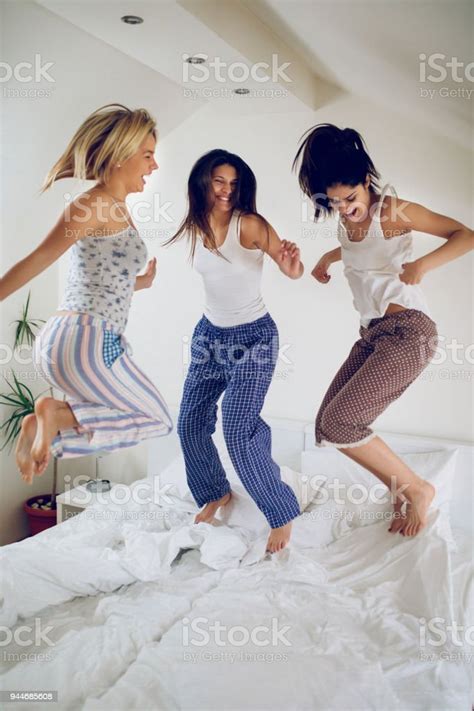 Playful Women Having Fun At Slumber Party Jumping On Bed Stock Photo