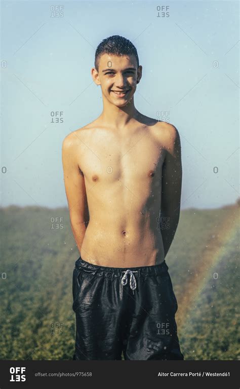 Shirtless Teenage Boy Enjoying Sprinkler In Farm Against Clear Sky