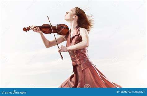 Woman Violinist In Red Dress Playing Melody Against Cloudy Sky Stock