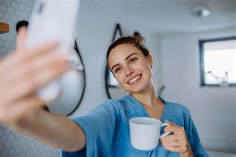 Young Woman Taking Selfie In Bathroom Enjoying Cup Of Coffee Stock