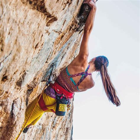 a woman climbing up the side of a rock with her hands in the air while wearing yellow pants