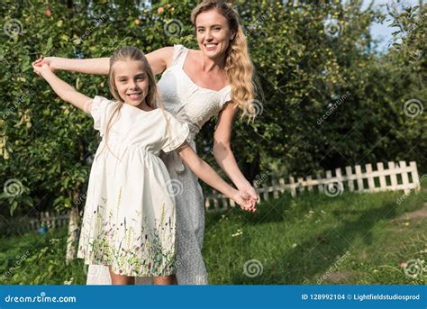 Attractive Mother And Adorable Daughter In White Dresses Holding Hands
