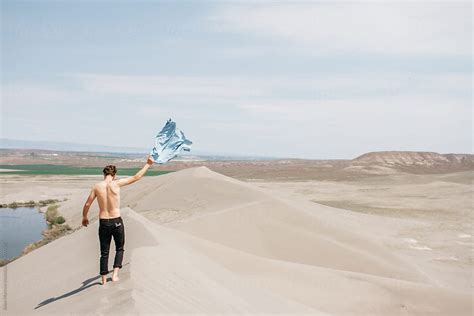 Young Man Waves Shirt In The Air While Topless In Desert Sand Dune Del Colaborador De Stocksy