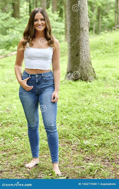 Gorgeous Young Woman In Blue Jeans And White Tank Top Poses Outside