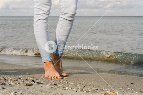 Female Feet In Jeans Barefoot Walk On The Sea Water On The Beach
