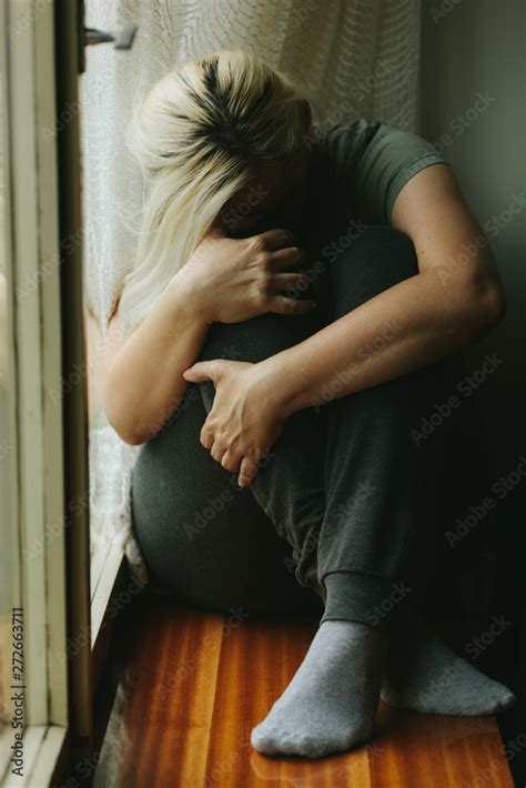 Blonde Woman Sitting On A Windowsill Hugging Herself In A Fetal Position Sad Lonely And