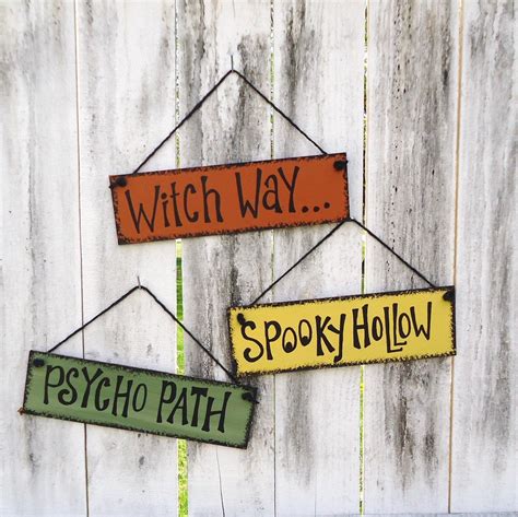 Two Wooden Signs Hanging On A White Fence That Say Witch Way And Spooky