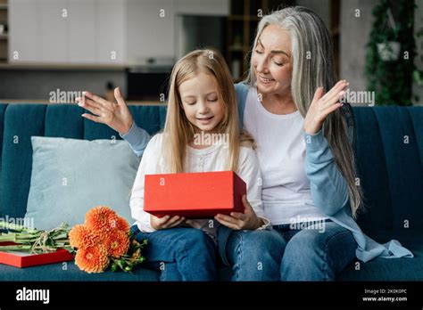 cheerful caucasian small girl opens t box with retired granny with bouquet of flowers and