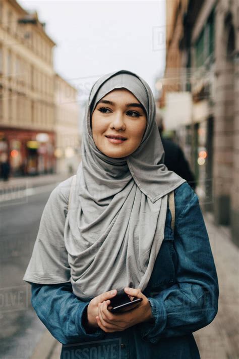 Young Muslim Woman Wearing Hijab Walking With Mobile Phone On Sidewalk
