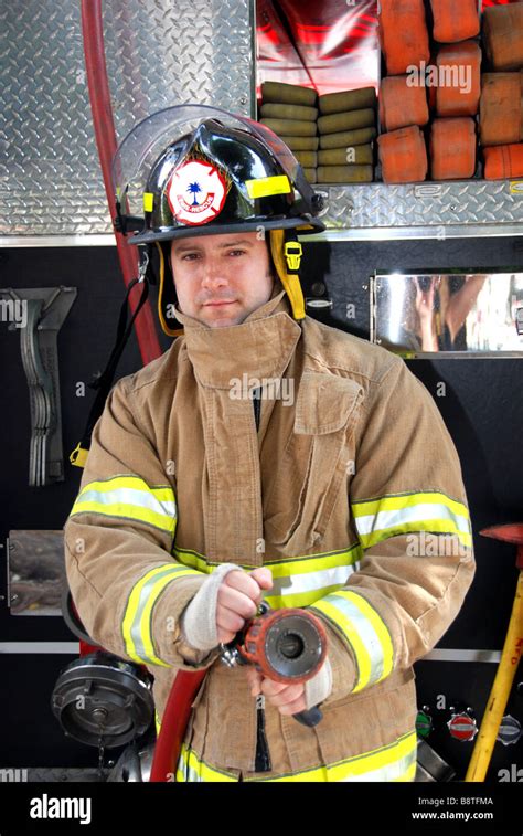 Male Firefighter Holding Fire Hose In Front Of Fire Truck Wearing
