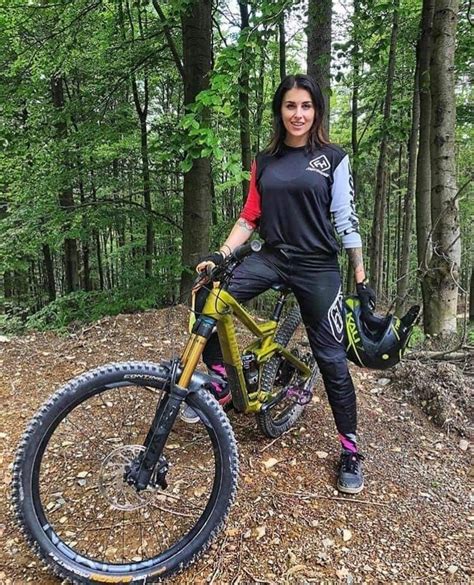 A Woman Standing Next To Her Bike In The Woods