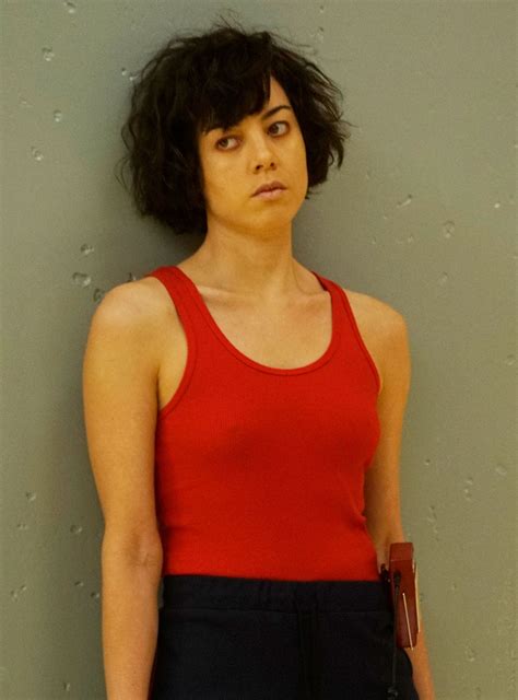 A Woman In A Red Tank Top Standing Next To A Wall With Her Hand On Her Hip