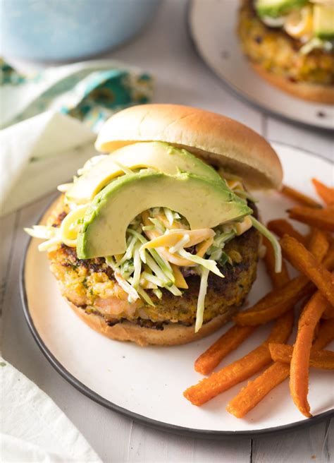 A Burger With Lettuce Avocado And Shredded Cheese On A Plate Next To