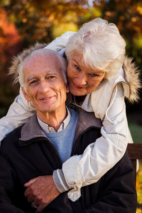 Elderly Woman Hugs Her Husband Sitting Bench Looking Camera Stock